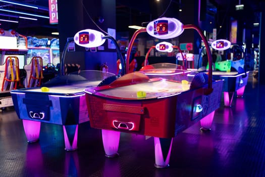 Air hockey tables illuminated neon light children's entertainment center, accompanied by various gaming machines in an arcade.