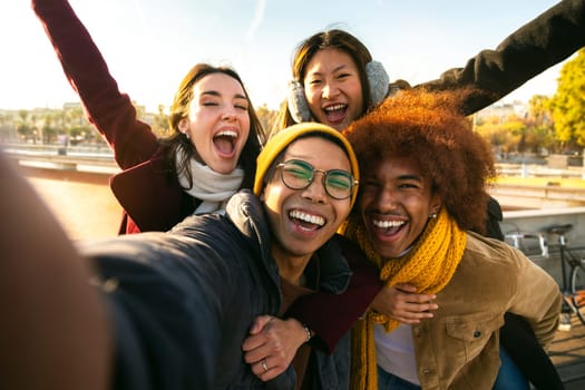Selfie of multi-ethnic cheerful friends enjoying sunny winter day outdoors. Group of diverse people looking at camera smiling. Lifestyle concept.