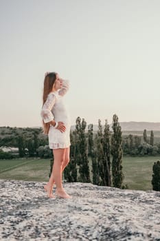 Romantic beautiful bride in white dress posing with sea and mountains in background. Stylish bride standing back on beautiful landscape of sea and mountains on sunset