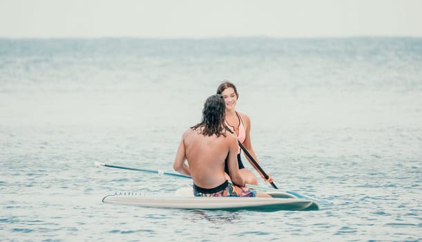 Sea woman and man on sup. Silhouette of happy young woman and man, surfing on SUP board, confident paddling through water surface. Idyllic sunset. Active lifestyle at sea or river