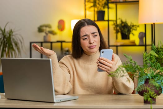 Sad displeased Caucasian woman use smartphone typing browsing, loses becoming surprised sudden lottery game results bad news fortune loss fail deadline virus crisis. Young girl at home office at table