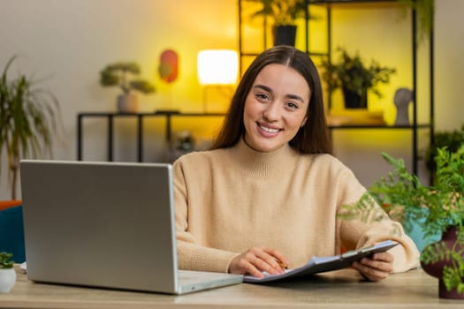 Happy young woman freelancer work with documents from home analyzing information read business papers prepare financial report. Girl winner satisfied by good victory success news on laptop. Copy-space