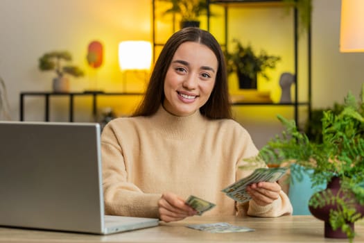 Planning budget. Rich smiling woman counting money cash use laptop computer calculate domestic bills at home table. Caucasian girl satisfied of income salary earnings money for planned vacation gifts