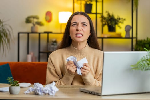 Angry furious Caucasian young woman throwing crumpled paper nervous breakdown at work stress management mental distress problems losing temper reaction on failure. Girl sitting at home room at table