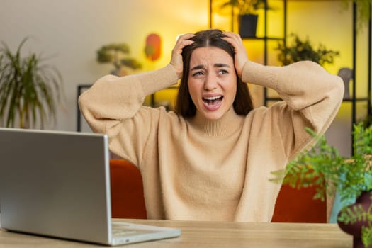 Aggressive Caucasian young woman screams from stress tension problems panic horror hopelessness fear surprise shock expresses gestures rage, nervous. Furious adult girl sitting at home office at table