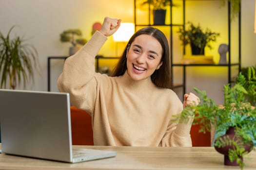 Happy Caucasian woman shouting celebrating success winning goal achievement good news lottery luck victory watching TV championship play game at home apartment. Girl in office room sits at table