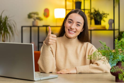 Like. Happy excited Caucasian woman looking approvingly at camera showing thumbs up like sign positive something good great news positive feedback. Girl sits at home office room at table. Copy-space