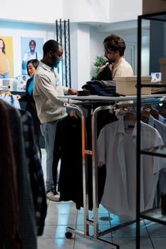 Clothing store employee assisting customer in selecting fashionable apparel, offering guidance on style. Boutique worker showcasing jacket to caucasian client and giving advice