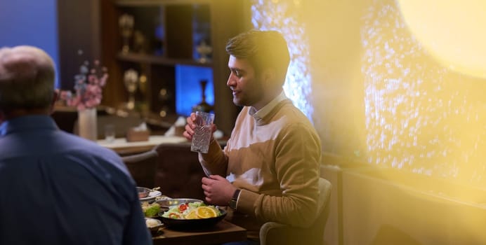 A son and his elderly father engage in heartfelt conversation while patiently awaiting their iftar meal, fostering intergenerational bonding and cherished moments of family connection.