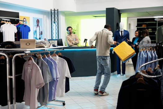 Clothing store excited client dancing with bags after buying trendy apparel with discount. Happy satisfied african american man holding purchase packages and enjoying shopping in boutique