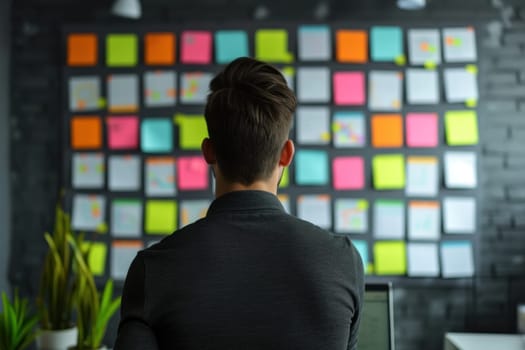 Back view of Businessman check week plan attached on big wall with paper notes. Generative AI.