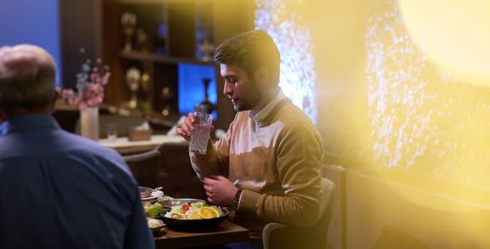 A son and his elderly father engage in heartfelt conversation while patiently awaiting their iftar meal, fostering intergenerational bonding and cherished moments of family connection.