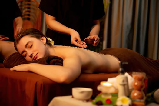 Couple customer having exfoliation treatment in luxury spa salon with warmth candle light ambient. Salt scrub beauty treatment in Health spa body scrub. Quiescent