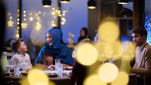 In a modern restaurant, an Islamic couple and their children joyfully await their iftar meal during the holy month of Ramadan, embodying familial harmony and cultural celebration amidst the contemporary dining ambiance.