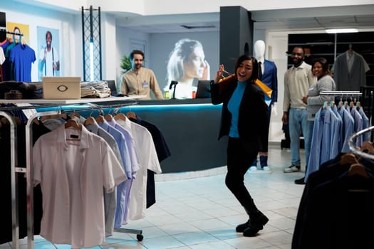 Cheerful smiling shopaholic dancing after making successful purchase in clothing store. Fashion boutique satisfied asian woman customer holding shopping bags in department mall