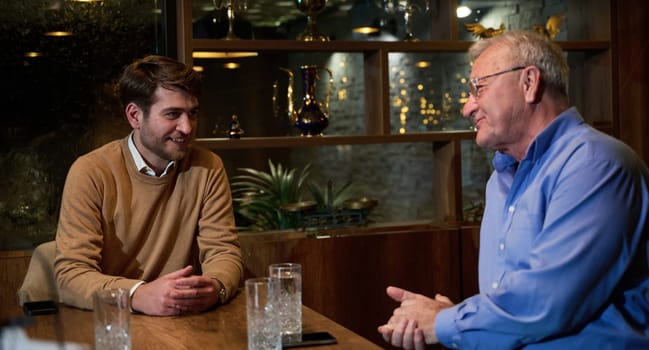 A son and his elderly father engage in heartfelt conversation while patiently awaiting their iftar meal, fostering intergenerational bonding and cherished moments of family connection.