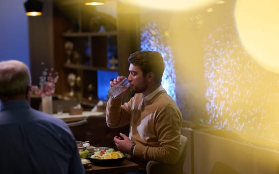 A son and his elderly father engage in heartfelt conversation while patiently awaiting their iftar meal, fostering intergenerational bonding and cherished moments of family connection.