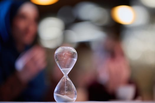 A symbolic hourglass counts down the time to iftar meal, while in the background, an Islamic family devoutly prays, capturing a poignant moment of spiritual connection and anticipation during Ramadan.