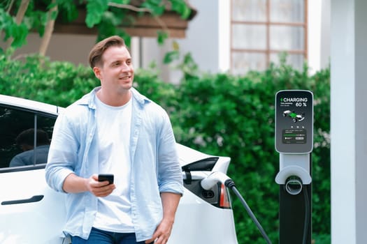 Modern eco-friendly man recharging electric vehicle from home EV charging station. Innovative EV technology utilization for tracking energy usage to optimize battery charging at home. Synchronos