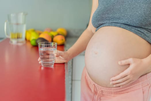 Embracing the vital benefits of water during pregnancy, a pregnant woman stands in the kitchen with a glass, highlighting hydration's crucial role in maternal well-being.