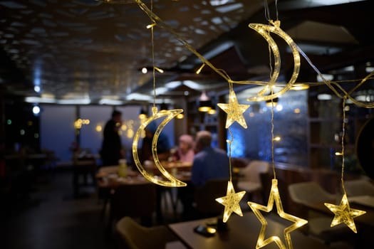 In a modern restaurant, the ambiance is transformed by the presence of sparkling Islamic symbolic Ramadan decorations, creating a festive and culturally rich atmosphere.