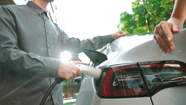 EV electric car charging in green sustainable city outdoor garden in summer shows lifestyle of young couple in urban sustainability green clean rechargeable energy of electric vehicle innards