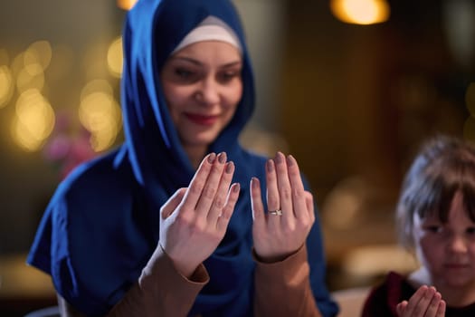 In a modern restaurant, a beautiful hijab-wearing woman prays with her hands raised, epitomizing grace, serenity, and spiritual devotion.