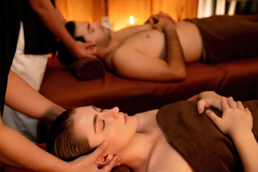 Couple customer enjoying relaxing anti-stress head massage and pampering facial beauty skin recreation leisure in warm candle lighting ambient salon spa in luxury resort or hotel. Quiescent