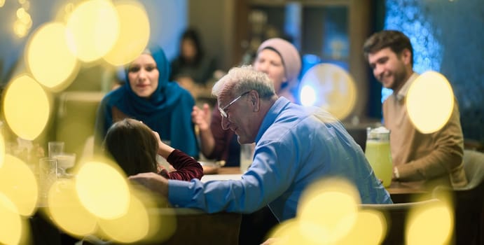 Grandparents arrive at their children's and grandchildren's gathering for iftar in a restaurant during the holy month of Ramadan, bearing gifts and sharing cherished moments of love, unity, and cultural exchange, as they eagerly await their meal together.