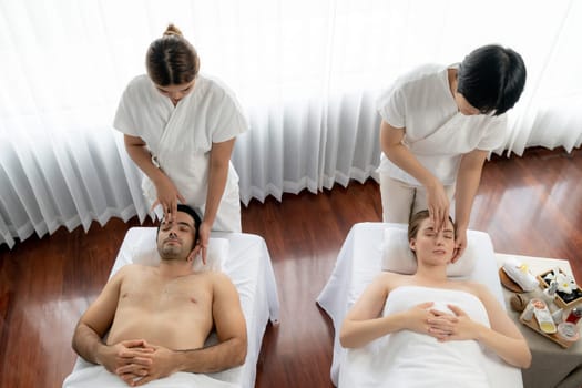 Caucasian couple enjoying relaxing anti-stress head massage and pampering facial beauty skin recreation leisure in dayspa modern light ambient at luxury resort or hotel spa salon. Quiescent
