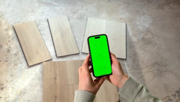 Hands Holding Device with Green Chroma Key Screen above Luxury Vinyl Wood Samples, Laminate On Floor In House. Choosing, Selecting Waterproof Flooring. Home Reconstruction. Horizontal Plane.