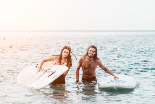 Sea woman and man on sup. Silhouette of happy young woman and man, surfing on SUP board, confident paddling through water surface. Idyllic sunset. Active lifestyle at sea or river