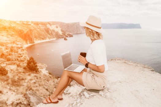 Digital nomad, Business woman working on laptop by the sea. Pretty lady typing on computer by the sea at sunset, makes a business transaction online from a distance. Freelance remote work on vacation