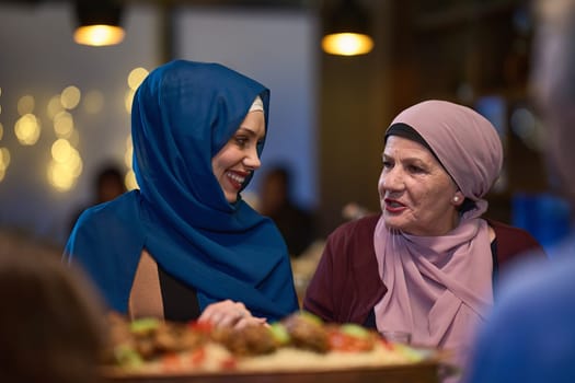 In a modern restaurant setting, a woman in hijab engages in conversation with her mother while they wait for the iftar meal, embodying familial bonding and cultural tradition during Ramadan