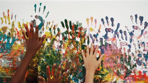 Happy diverse student hand placed on colorful stained wall. Closeup of multicultural hand or children with mixed races paint their hand print at art room. Background. Creative activity. Edification.