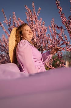 Woman blooming peach orchard. Against the backdrop of a picturesque peach orchard, a woman in a long pink dress and hat enjoys a peaceful walk in the park, surrounded by the beauty of nature