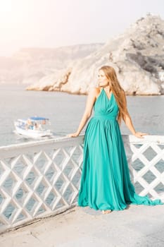 Woman sea trevel green dress. Side view a happy woman with long hair in a long mint dress posing on a beach with calm sea bokeh lights on sunny day. Girl on the nature on blue sky background