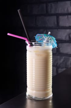 Close up of glass with white cocktail and straw. Protein shake on the counter in bar. Banks with sports nutrition on background. Fresh drink. Free space for text.