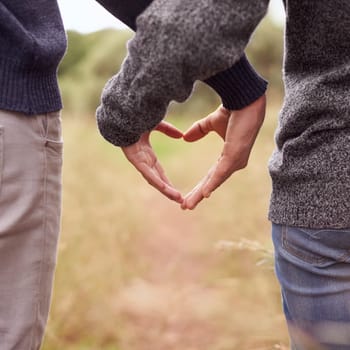 Heart hands, love and couple in the countryside together for hiking, romance or adventure closeup. Nature, emoji or symbol with man and woman dating outdoor for anniversary or honeymoon from back.