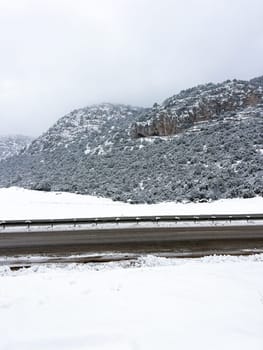 Road passing a rocky mountain on a snowy winter day