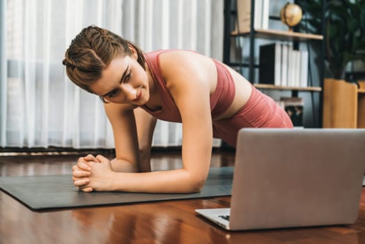 Flexible and dexterity woman in sportswear doing yoga position in meditation posture on exercising mat at home. Healthy gaiety home yoga online training session with peaceful mind and serenity.