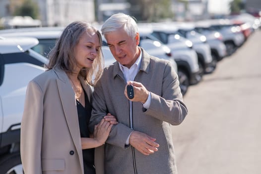 Mature Caucasian couple standing by a car outdoors. Elderly man holding car keys