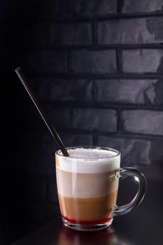 A glass of Latte macchiato with syrup and straw on black table with brick wall behind