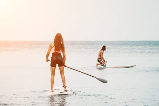 Sea woman and man on sup. Silhouette of happy young woman and man, surfing on SUP board, confident paddling through water surface. Idyllic sunset. Active lifestyle at sea or river