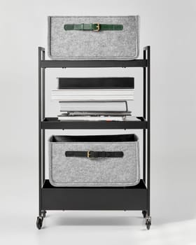 Modern metal office trolley with gray felt storage drawers decorated with green and black leather handles, and fashion photography books on shelves. Stylish interior accessories for organizing space