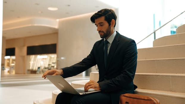 Skilled investor working or planing strategy by using laptop at stair. Professional business man wearing suit while working and typing data analysis by using laptop at modern hotel. Exultant.