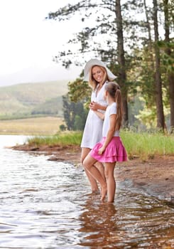 Mother, daughter and happiness outdoor in river for bonding, support or holding hands on holiday in nature. Family, woman and girl child with smile or adventure on vacation, travel and lake with love.