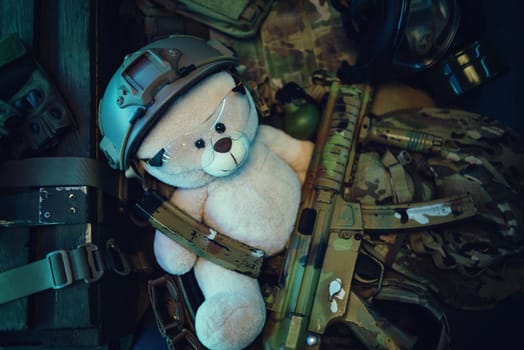 teddy bear in a military helmet among a pile of military ammunition, a rifle, grenades, a bulletproof vest, a helmet and other tactical airsoft items