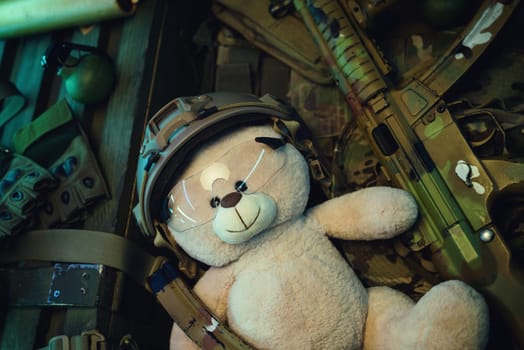 teddy bear in a military helmet among a pile of military ammunition, a rifle, grenades, a bulletproof vest, a helmet and other tactical airsoft items