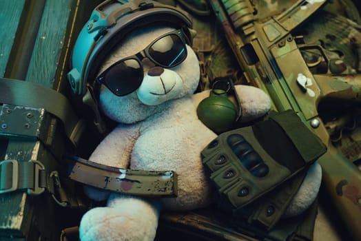 teddy bear in a military helmet among a pile of military ammunition, a rifle, grenades, a bulletproof vest, a helmet and other tactical airsoft items